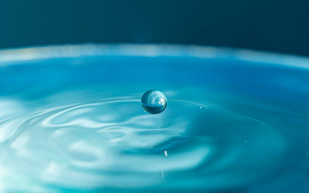 a single water droplet suspended just above a rippling blue surface moments before it lands